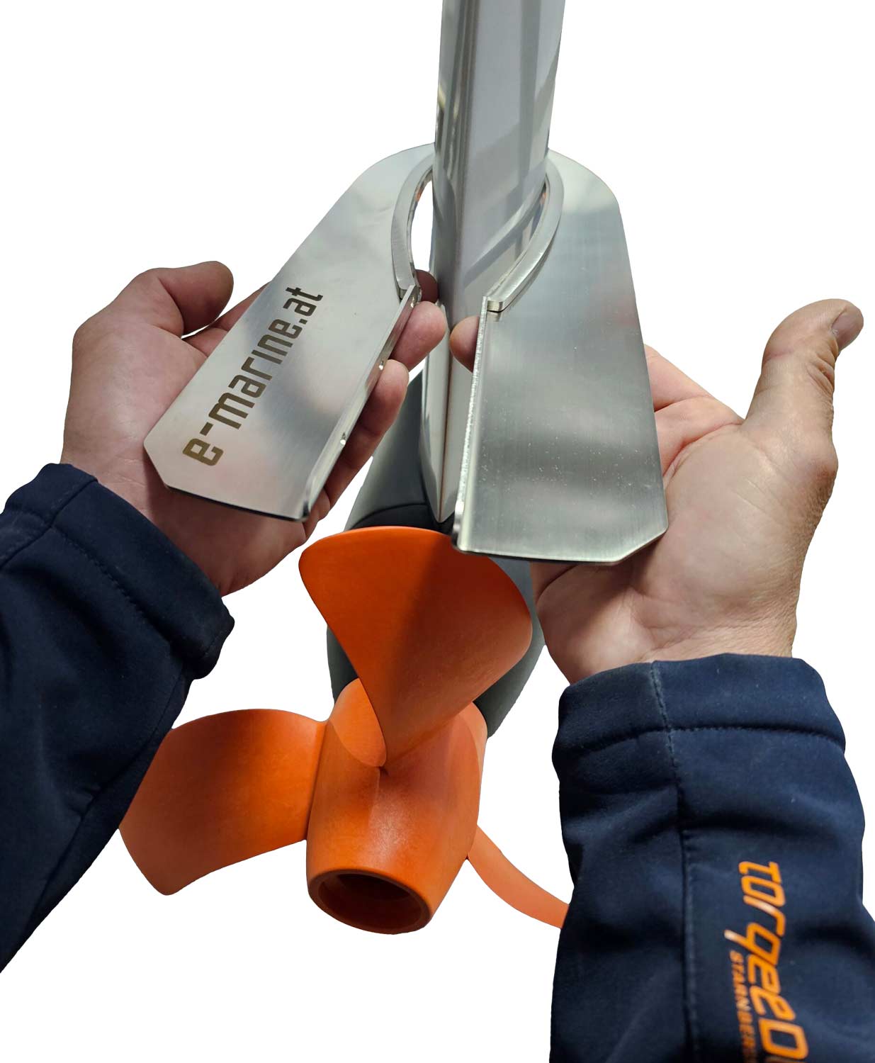Close-up of hands holding a metal mounting bracket labeled e-marine.at near an orange boat propeller, with a white background. The person is wearing a dark blue jacket with Torqeedo printed on the sleeve.